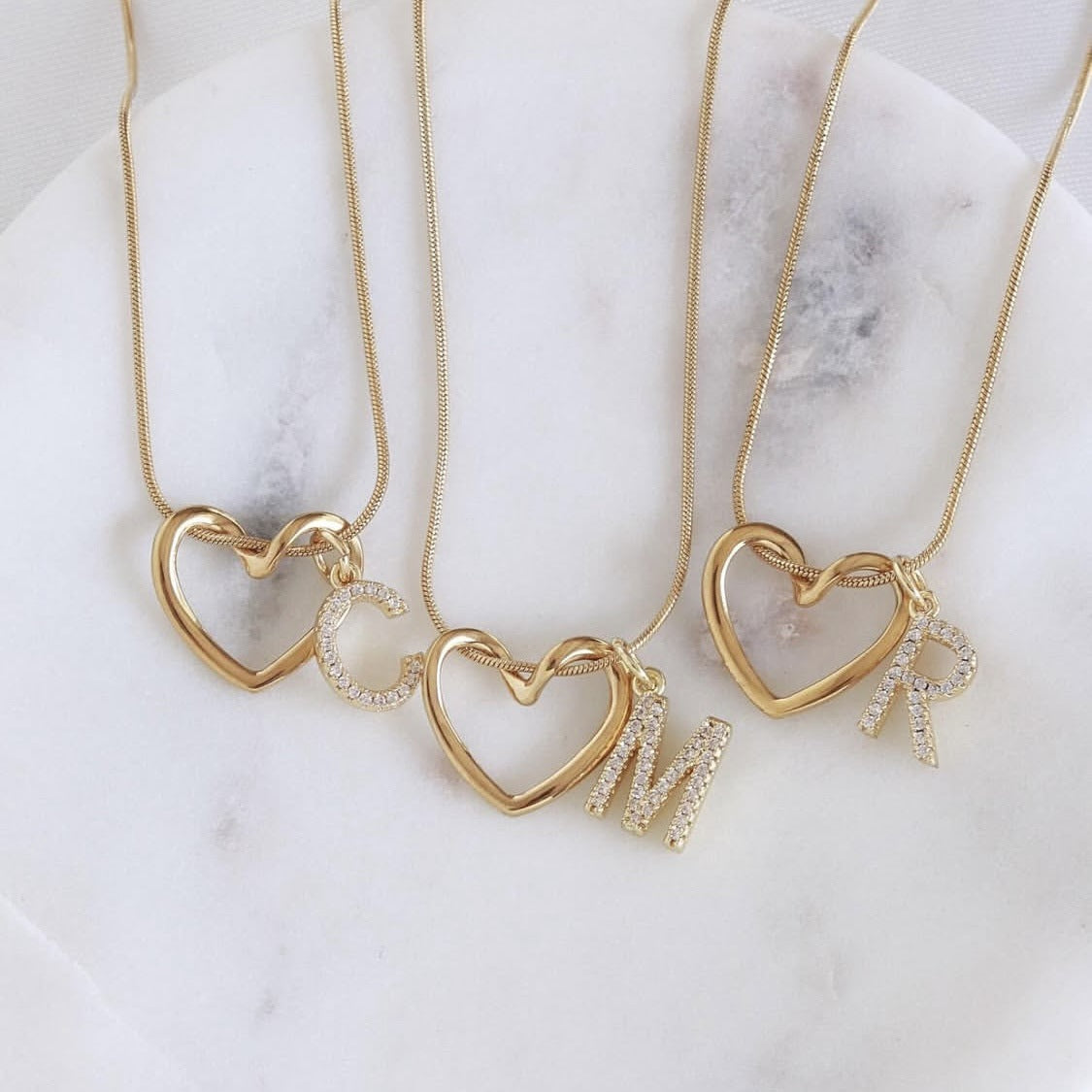 Three Keepsake Heart necklaces with initials C, M and R on marble