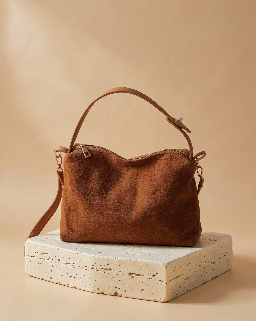 The Soft Zip crossbody in brown on a travertine block